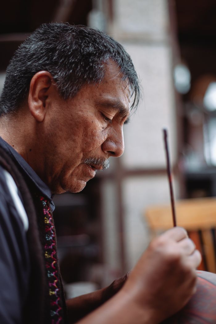 services-img Side view of an elderly man concentrating on his intricate art creation with a wooden stick.
